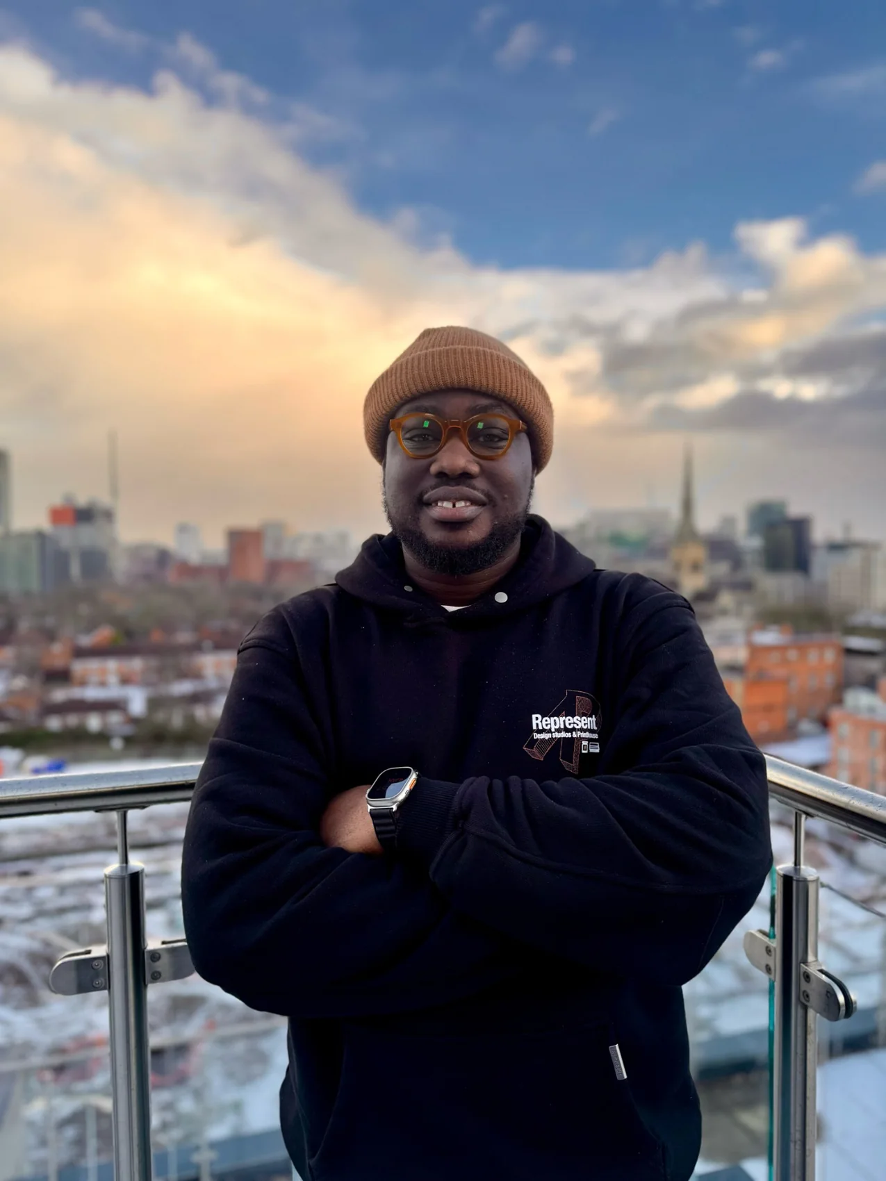 Portrait of Mayowa on a rooftop, arms crossed, in a brown beanie